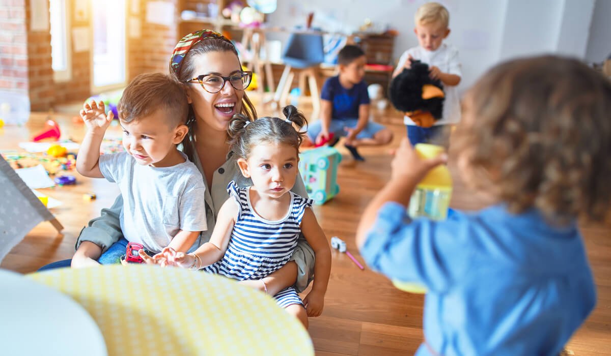 A home daycare provider laughing and playing with toddlers in a bright playroom